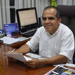 Hombre sentado frente a un escritorio sosteniendo un documento y un lapicero.