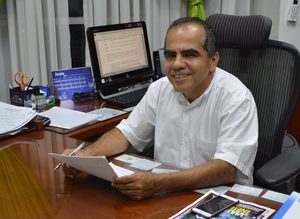 Hombre sentado frente a un escritorio sosteniendo un documento y un lapicero.