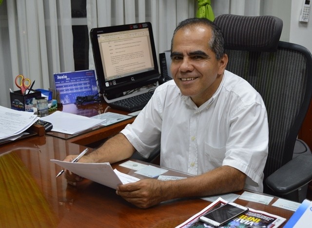 Hombre sentado frente a un escritorio sosteniendo un documento y un lapicero.